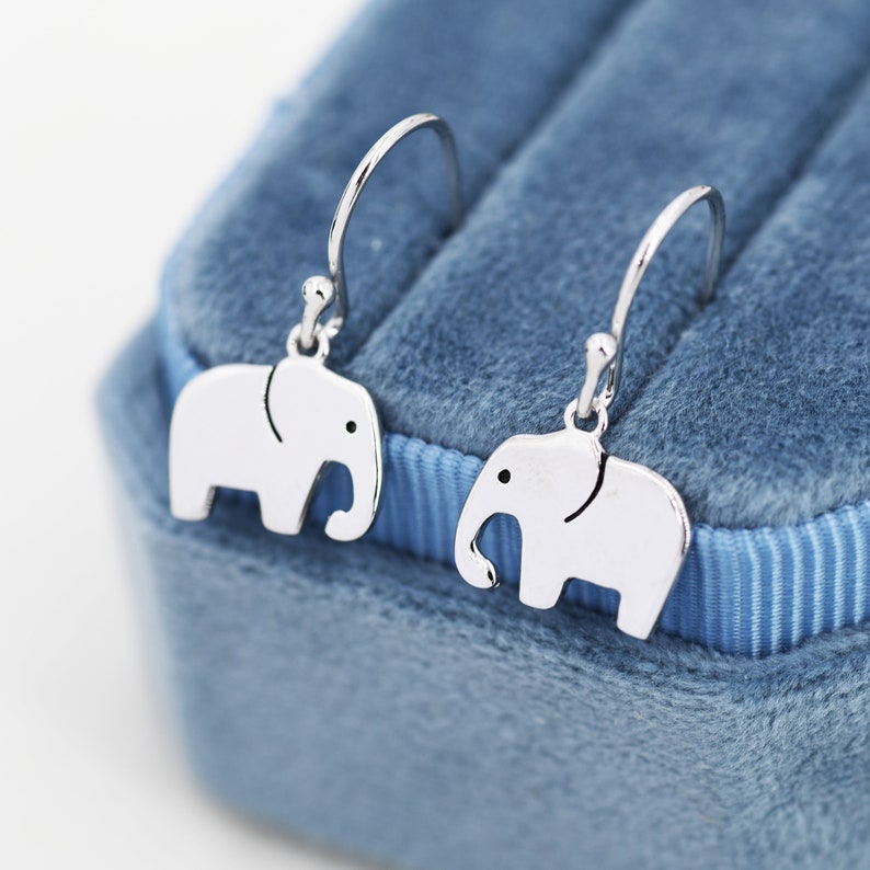 May include: A pair of silver elephant dangle earrings on a blue velvet background.