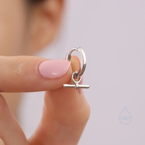 May include: A silver hoop earring with a small silver bar charm hanging from it.