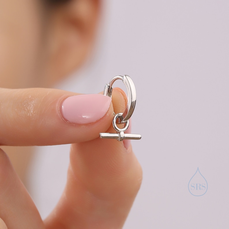 May include: A silver hoop earring with a small silver bar charm hanging from it.