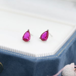 May include: A pair of silver teardrop earrings with bright pink gemstones.