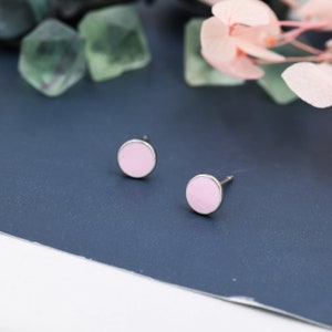 May include: A pair of small, round earrings with a pink enamel finish and silver metal settings.