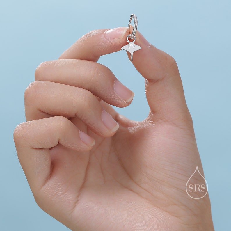 May include: Silver hoop earring with a small silver stingray charm hanging from it.