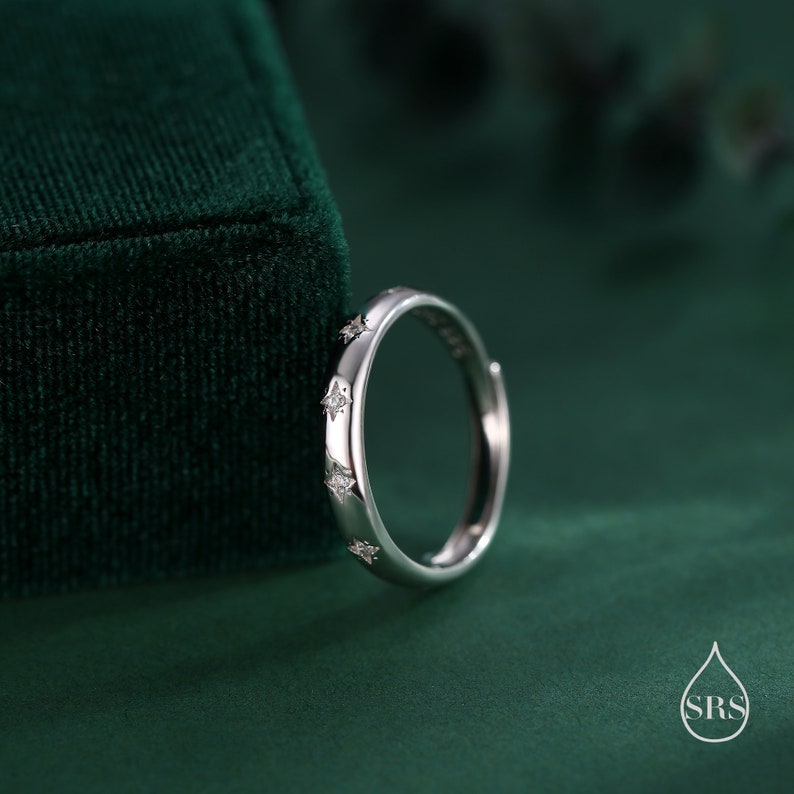 May include: A silver ring with small, clear stones set in the shape of stars around the band.
