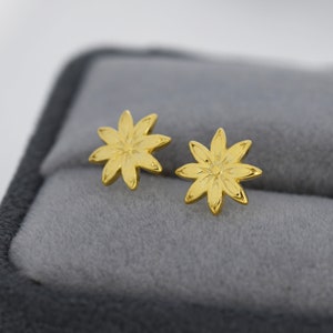 May include: A pair of gold-toned flower-shaped stud earrings. The earrings are small and delicate, with a simple design.
