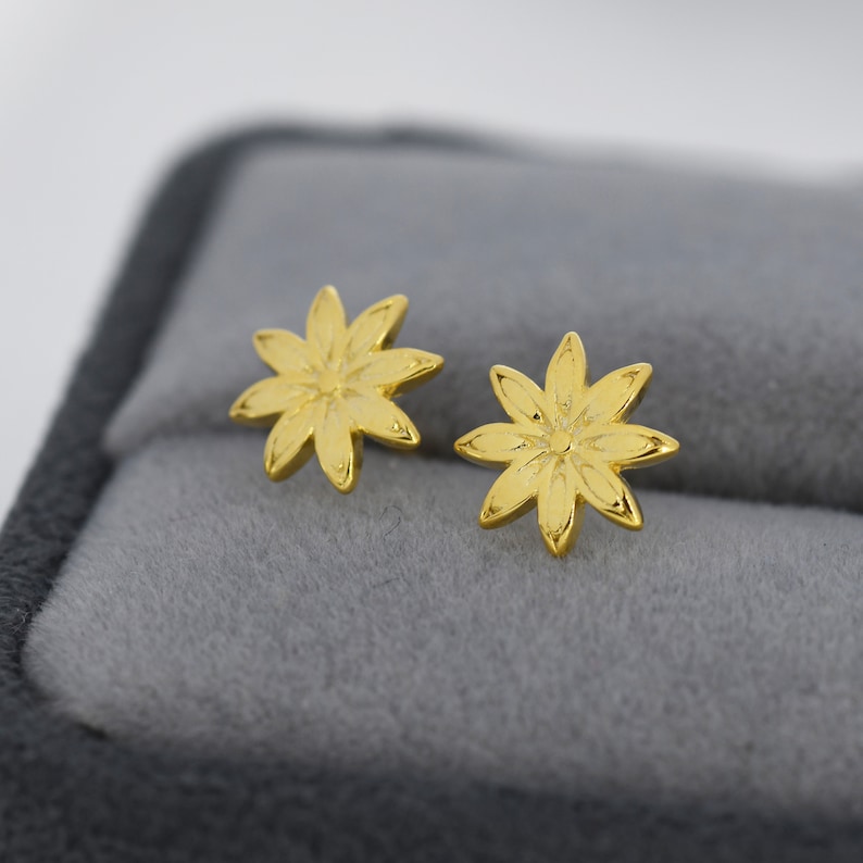May include: A pair of gold-toned flower-shaped stud earrings. The earrings are small and delicate, with a simple design.