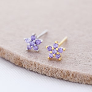 May include: Two small flower-shaped earrings with purple gemstones. One earring has a silver post and the other has a gold post.