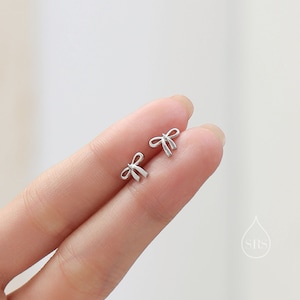 Puede incluir: Un par de pendientes de bot&oacute;n de plata en forma de lazo. Los pendientes son peque&ntilde;os y delicados, y son perfectos para a&ntilde;adir un toque de elegancia a cualquier atuendo.