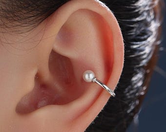 May include: A silver-toned ear cuff featuring a single white spherical pearl accent. The smooth, polished metal band curves around the cartilage of the ear, providing a minimalist look that secures firmly without the need for a piercing.