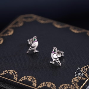 May include: A pair of silver dove earrings with green and purple enamel accents. The doves are facing forward with their wings outstretched.