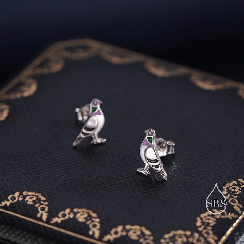 May include: A pair of silver dove earrings with green and purple enamel accents. The doves are facing forward with their wings outstretched.