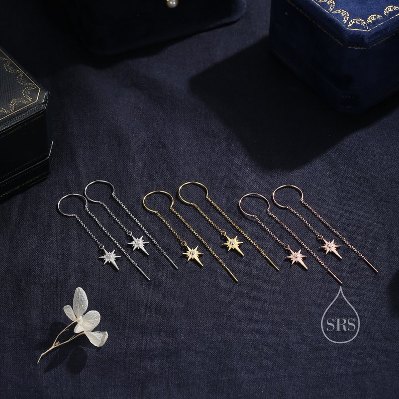 May include: Six pairs of dangle earrings with a starburst design featuring a single clear stone in the center. The earrings are available in silver, gold, and rose gold.