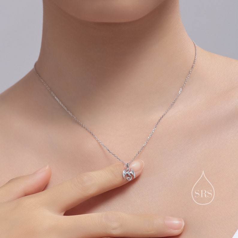 May include: A silver necklace with a small dragon pendant. The dragon is facing forward with its wings spread out.