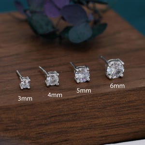 May include: Four silver-toned stud earrings with clear round stones in four-prong settings. The earrings are labelled with sizes 3mm, 4mm, 5mm, and 6mm, showing a progression in diameter from the smallest to the largest size in the set.