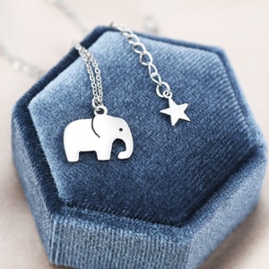 May include: A silver necklace with a small elephant charm and a star charm. The necklace is displayed on a blue velvet box.