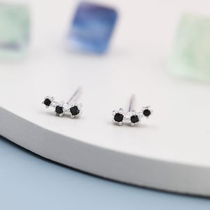 May include: A pair of silver stud earrings with three black gemstones arranged in a curved line.