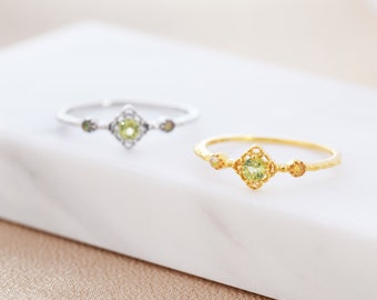May include: Two delicate rings with green gemstones set in intricate filigree designs. The ring on the left is silver with black accents, while the ring on the right is gold with yellow accents.