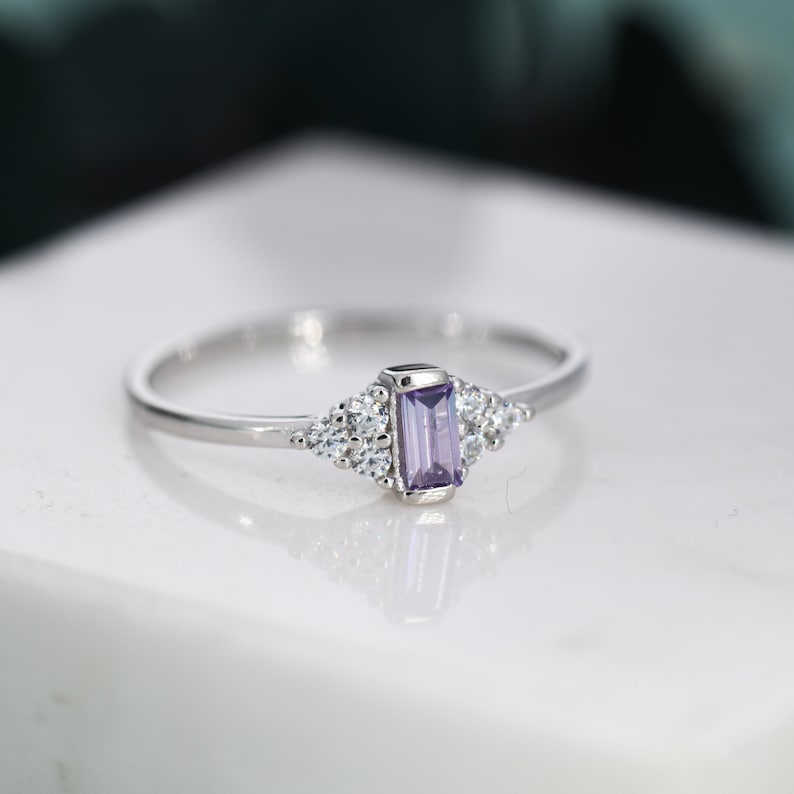 Puede incluir: Un anillo de plata con una piedra preciosa p&uacute;rpura y peque&ntilde;as piedras transparentes engastadas en un dise&ntilde;o delicado.