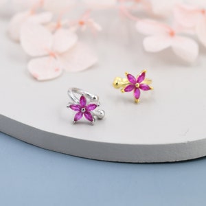 Könnte beinhalten: Zwei Ohrringe aus Silber und Gold mit rosa Blumenakzenten. Die Ohrringe liegen auf einer weißen Oberfläche.