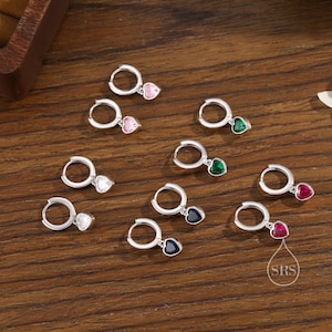 Peut inclure: Boucles d'oreilles créoles en argent avec des pierres précieuses en forme de cœur de différentes couleurs : rose, vert, rouge, blanc et bleu. Les boucles d'oreilles sont présentées sur une surface en bois, mettant en valeur leur design et leurs couleurs.