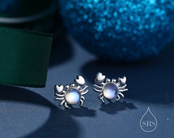 Könnte beinhalten: Ein Paar silberne Krebsohrringe mit schimmernden Mondstein-Akzenten. Die Ohrringe sind klein und zart und perfekt, um jedem Outfit einen Hauch von Verspieltheit zu verleihen.