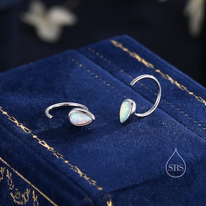 May include: A pair of silver hoop earrings with teardrop-shaped opal stones. The earrings are on a blue velvet background.