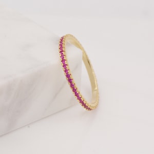 May include: A gold band ring with a row of small pink gemstones around the entire band.