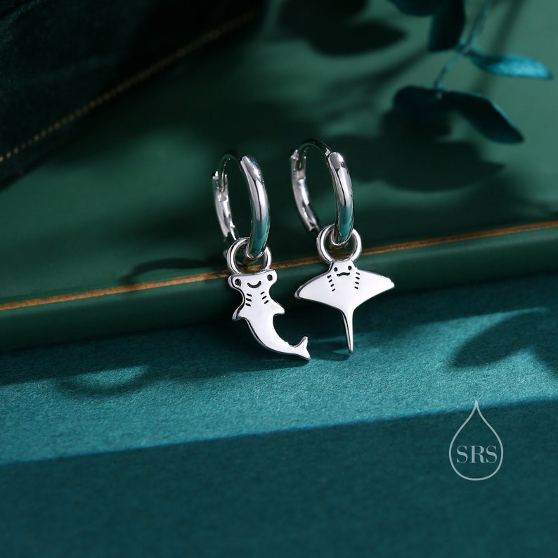 May include: A pair of silver hoop earrings with a hammerhead shark and a manta ray charm hanging from each hoop.