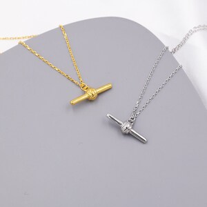 May include: Two delicate necklaces with a simple chain and a knot-shaped pendant. One necklace is gold and the other is silver.