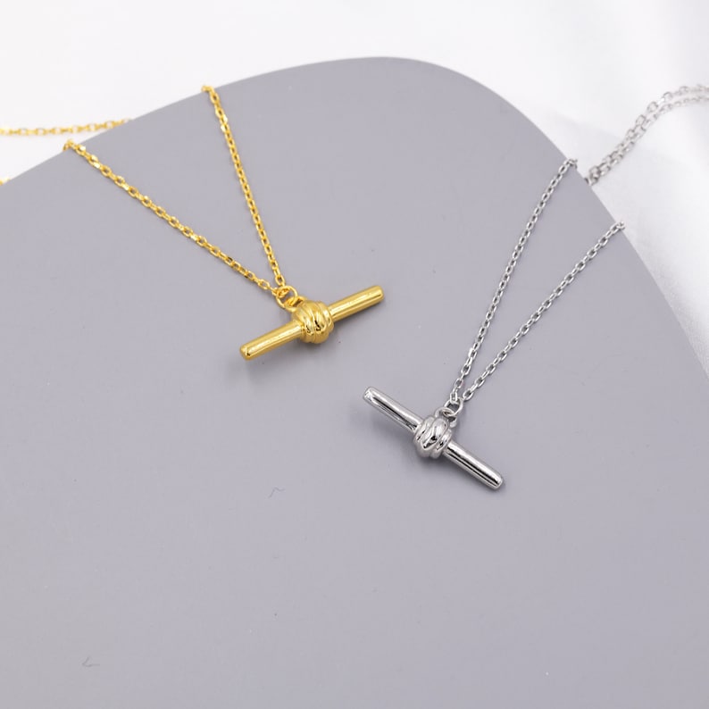 May include: Two delicate necklaces with a simple chain and a knot-shaped pendant. One necklace is gold and the other is silver.