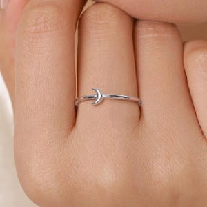 Könnte beinhalten: Ein silberner Ring mit einem Halbmond-Design. Der Ring ist dünn und filigran, mit dem Mond als zentralem Element. Der Ring wird an einem Finger getragen, was die schlichte Eleganz des Schmucks hervorhebt.