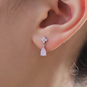 Puede incluir: Un par de pendientes de plata con un pequeño diseño de flor y una piedra de ópalo en forma de lágrima que cuelga de cada uno.