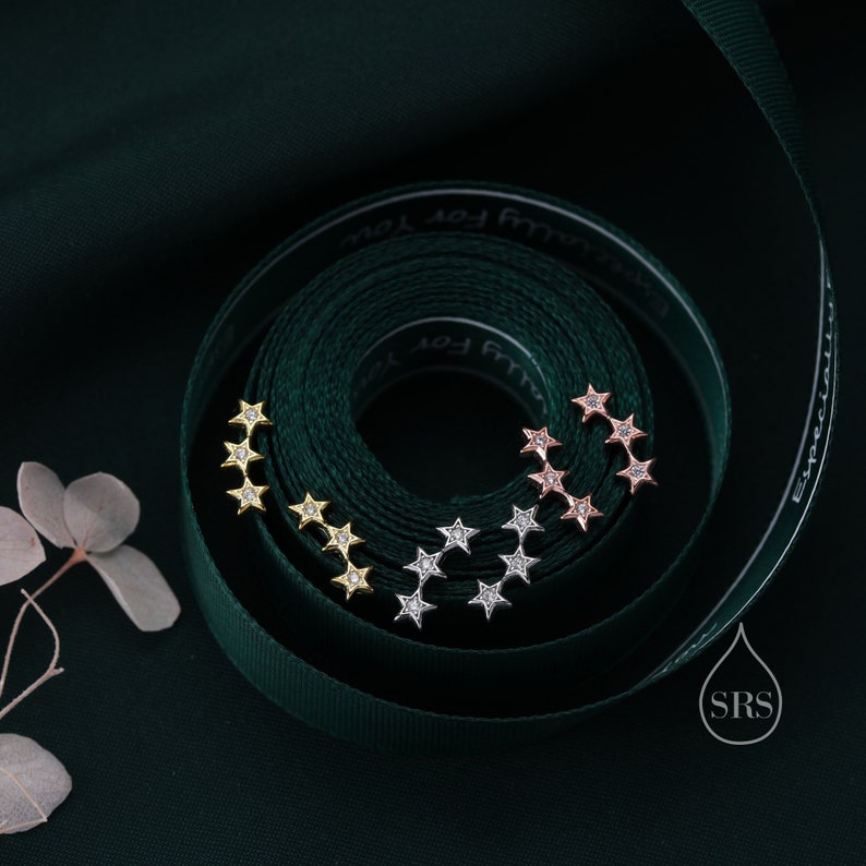 May include: Three sets of star-shaped earrings with clear cubic zirconia stones. The earrings are in gold, rose gold, and silver.