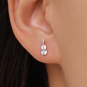 May include: A silver-colored violin-shaped stud earring. The earring is small and detailed, with the shape of a violin. The earring is worn on the earlobe.