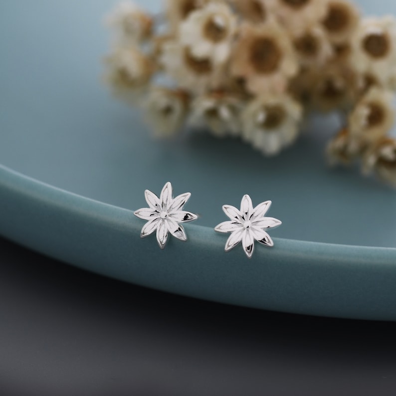 May include: A pair of silver flower-shaped stud earrings. The earrings are small and delicate, with a simple design.