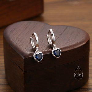 May include: A pair of silver hoop earrings with a dangling heart-shaped charm. Each charm features a blue gemstone.
