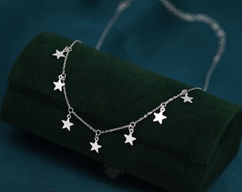 May include: A silver necklace with a delicate chain and multiple star-shaped pendants. The necklace is displayed on a green velvet box.