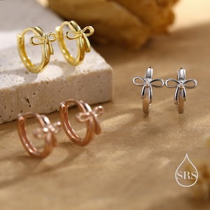 Puede incluir: Tres pares de pendientes de aro con diseño de lazo. Los pendientes son de oro, oro rosa y plata.