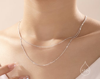 May include: A silver layered necklace with a delicate chain and a chain with small round beads. The necklace is worn by a person with fair skin.