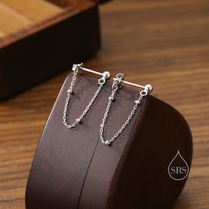 May include: A pair of silver earrings with a bar and a dangling chain with small beads. The earrings are displayed on a wooden surface.