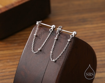 May include: A pair of silver earrings with a bar and a dangling chain with small beads. The earrings are displayed on a wooden surface.