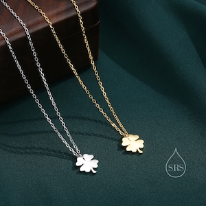 May include: Two delicate necklaces with four-leaf clover pendants. One necklace is silver and the other is gold. The necklaces are on a green background.