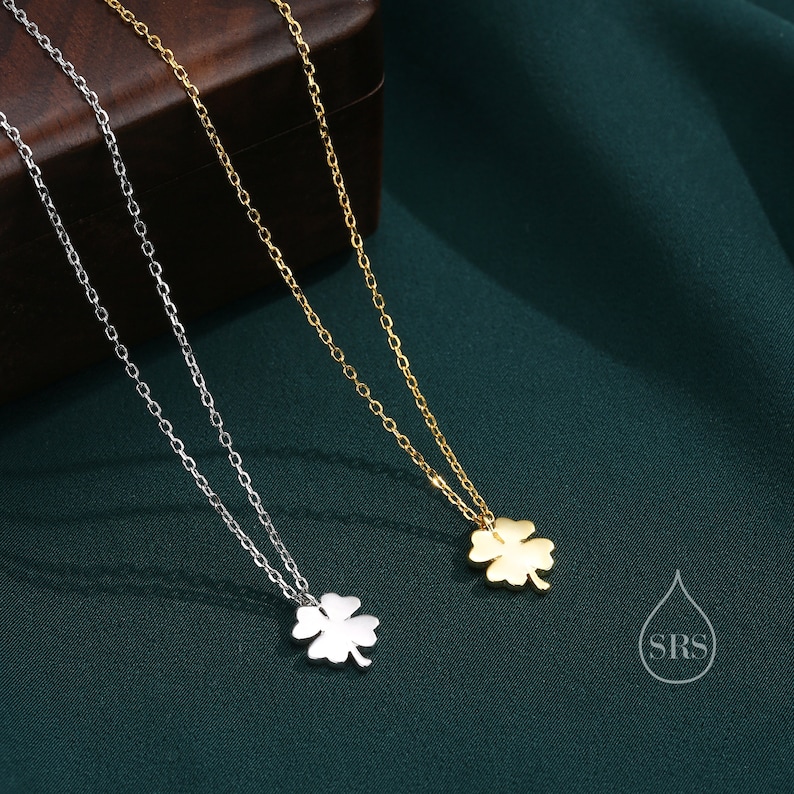 May include: Two delicate necklaces with four-leaf clover pendants. One necklace is silver and the other is gold. The necklaces are on a green background.