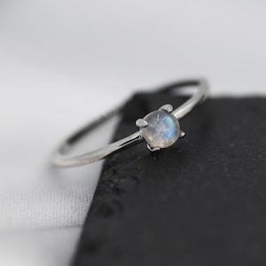 May include: A silver ring featuring a round, iridescent moonstone.