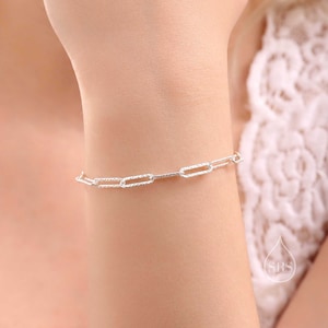 May include: A silver chain bracelet with a textured, rectangular link design.