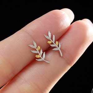May include: A pair of silver olive branch earrings with gold olive accents. The earrings are small and delicate.
