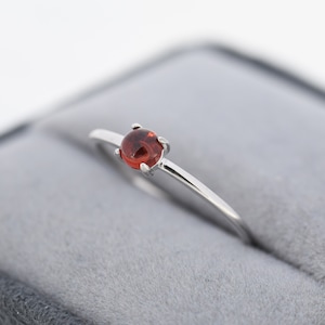 May include: A silver ring with a small, round, red gemstone.