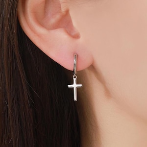 Puede incluir: Pendientes de aro de plata con un dije de cruz colgante.