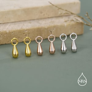 Könnte beinhalten: Sechs tropfenförmige Anhänger in Gold-, Roségold- und Silbertönen. Jeder Anhänger hat oben eine kleine Schlaufe. Die Anhänger sind auf einer grünen Oberfläche mit neutralem Hintergrund angeordnet.