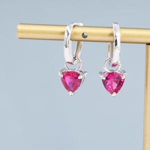 May include: A pair of silver hoop earrings with a dangling pink triangle-shaped gemstone.