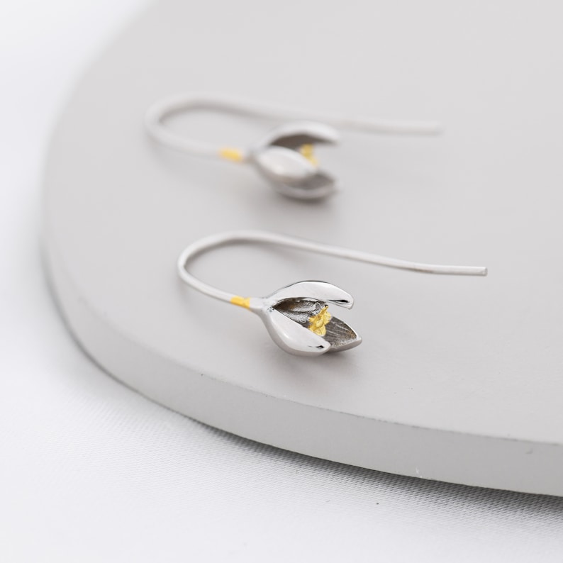 Puede incluir: Un par de pendientes de plata con forma de flor y un centro dorado. Los pendientes son delicados y tienen un dise&ntilde;o sencillo.